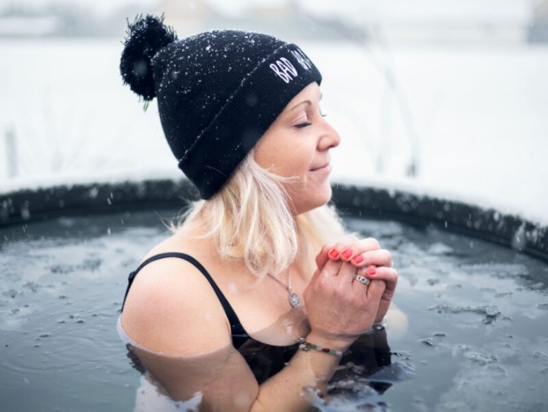 A woman with a hat on sits in an ice bath