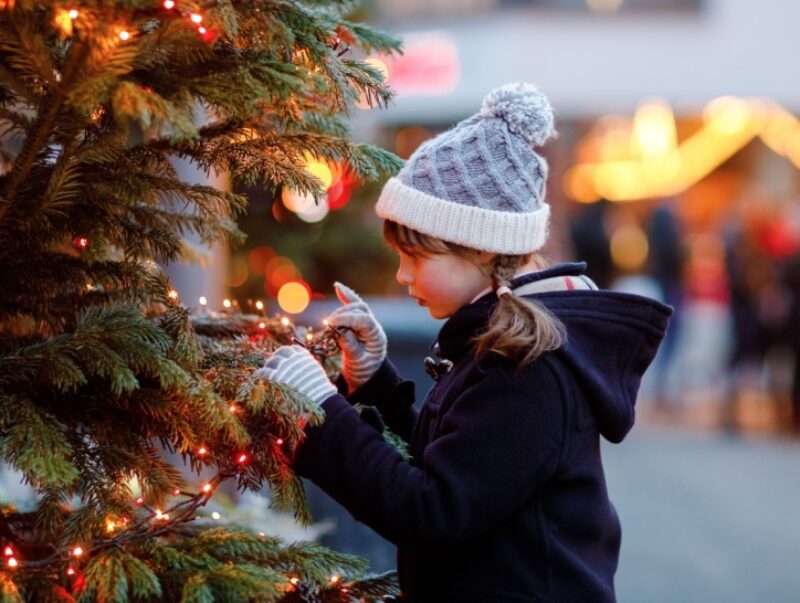 A child looking at a Christmas tree with a market in the background