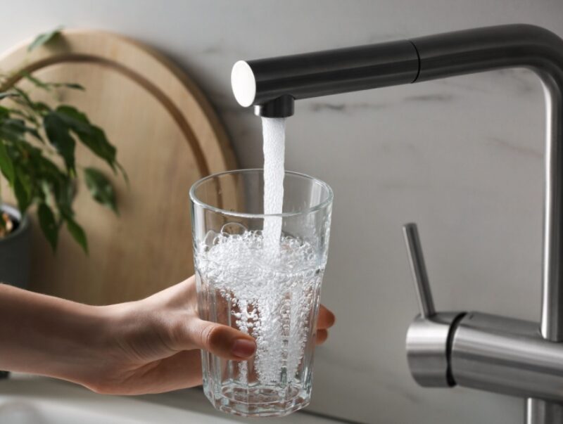 A person pouring a glass of water from a tap