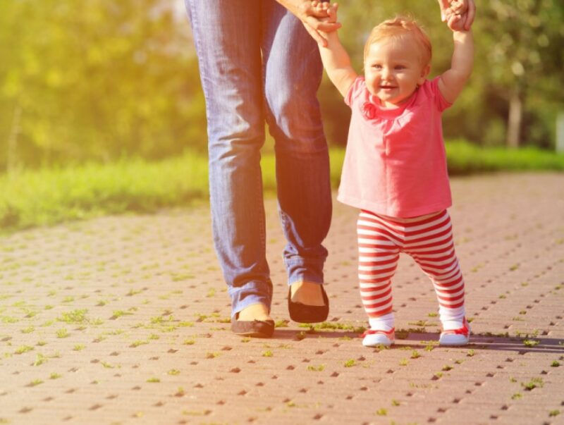 A parent holding a child’s hands as she learns to walk