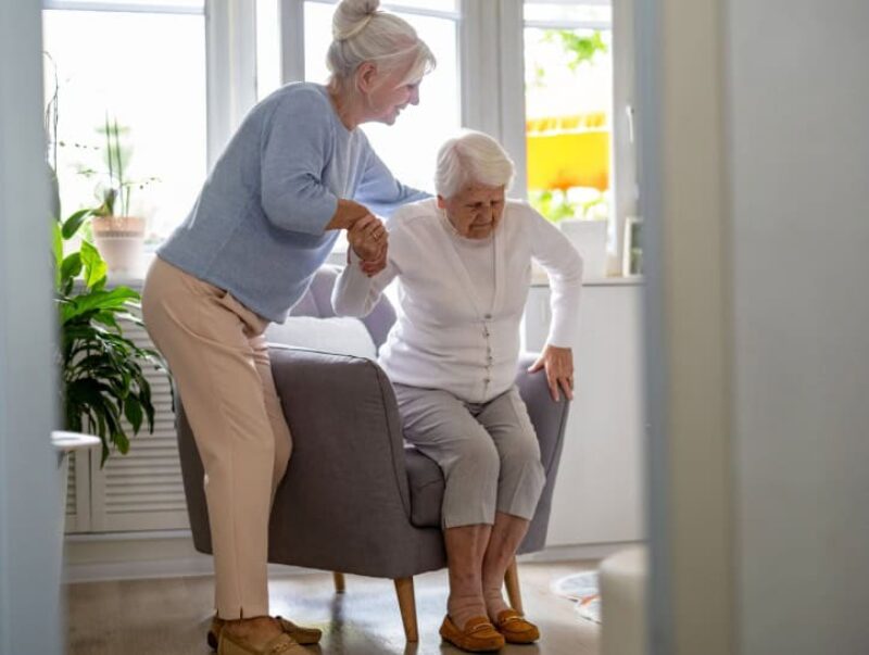 A woman helping her mother out of a chair