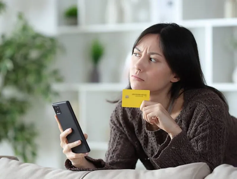 Woman looking at her phone and holding a credit card